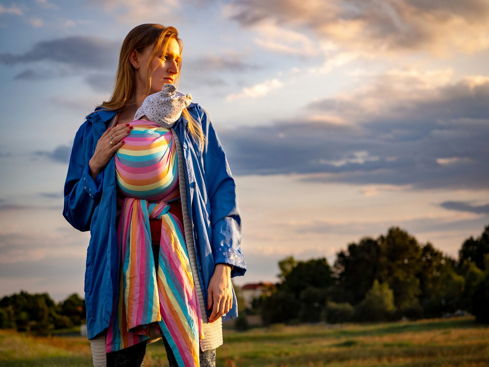 Una mamá al atardecer, cargando a su bebé en un portabebés de tela, caminando por un campo abierto