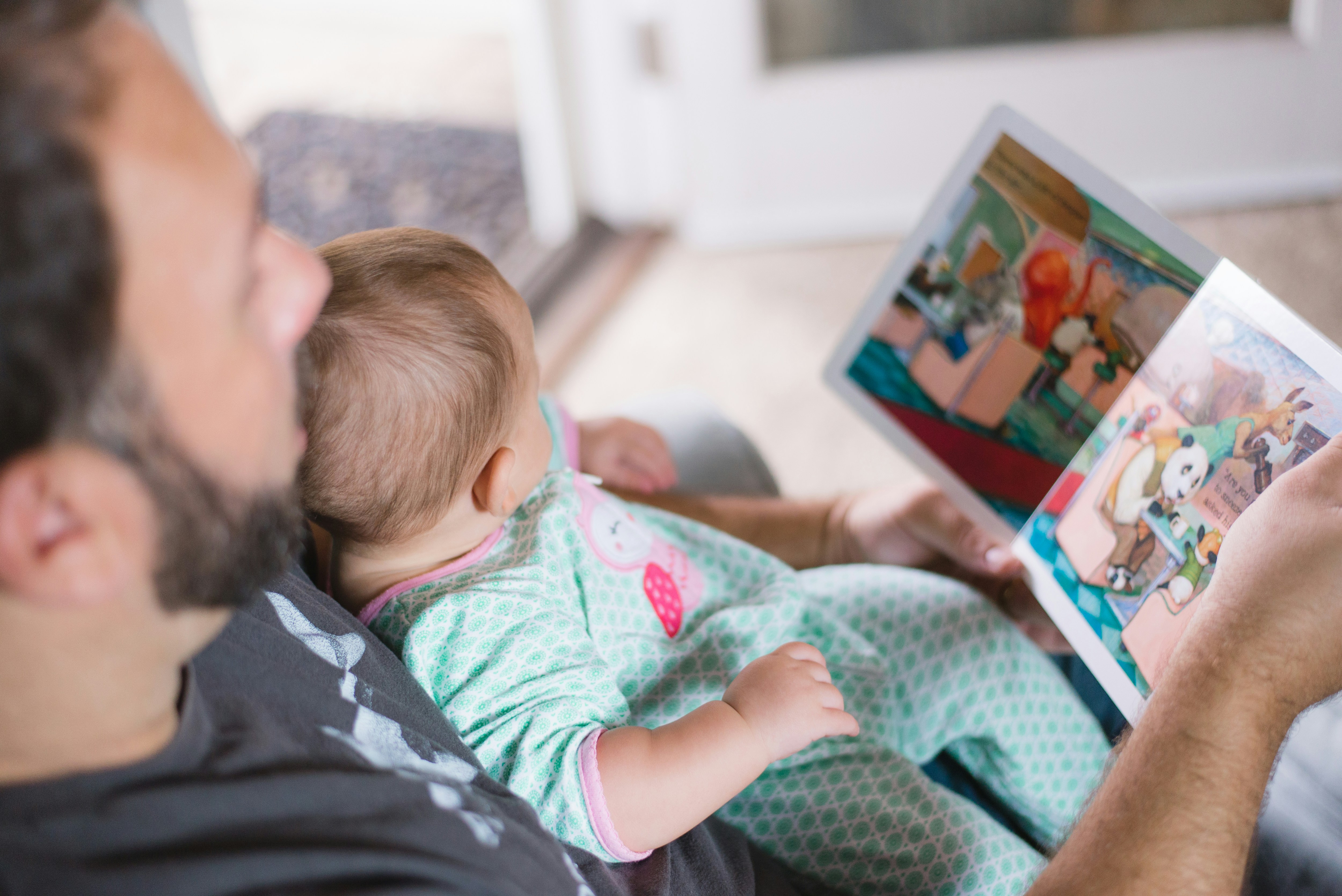 A dad reading a picture book with his baby on his lap