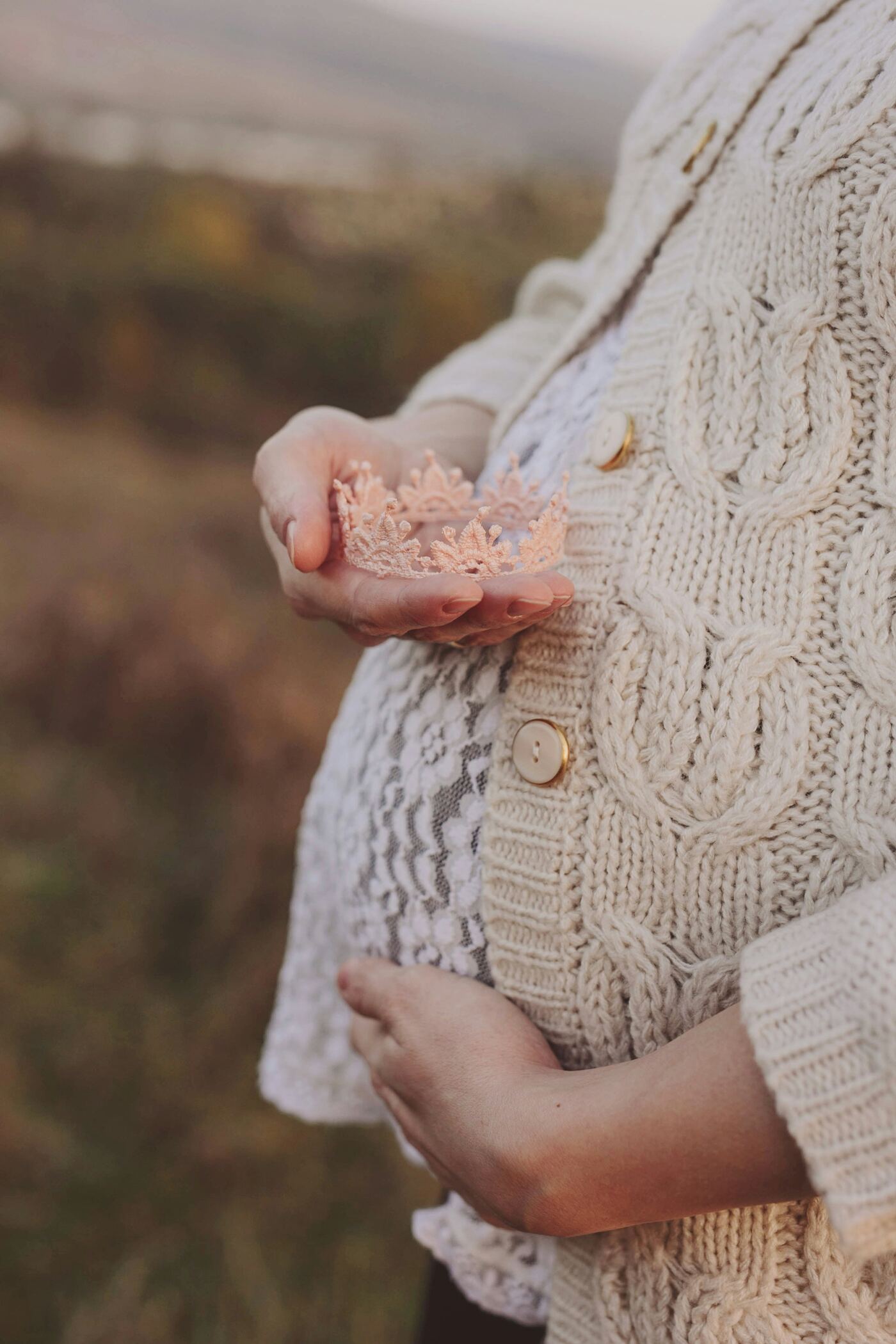 Expecting mother gently cradling a small lace crown against her belly, a quiet protective moment