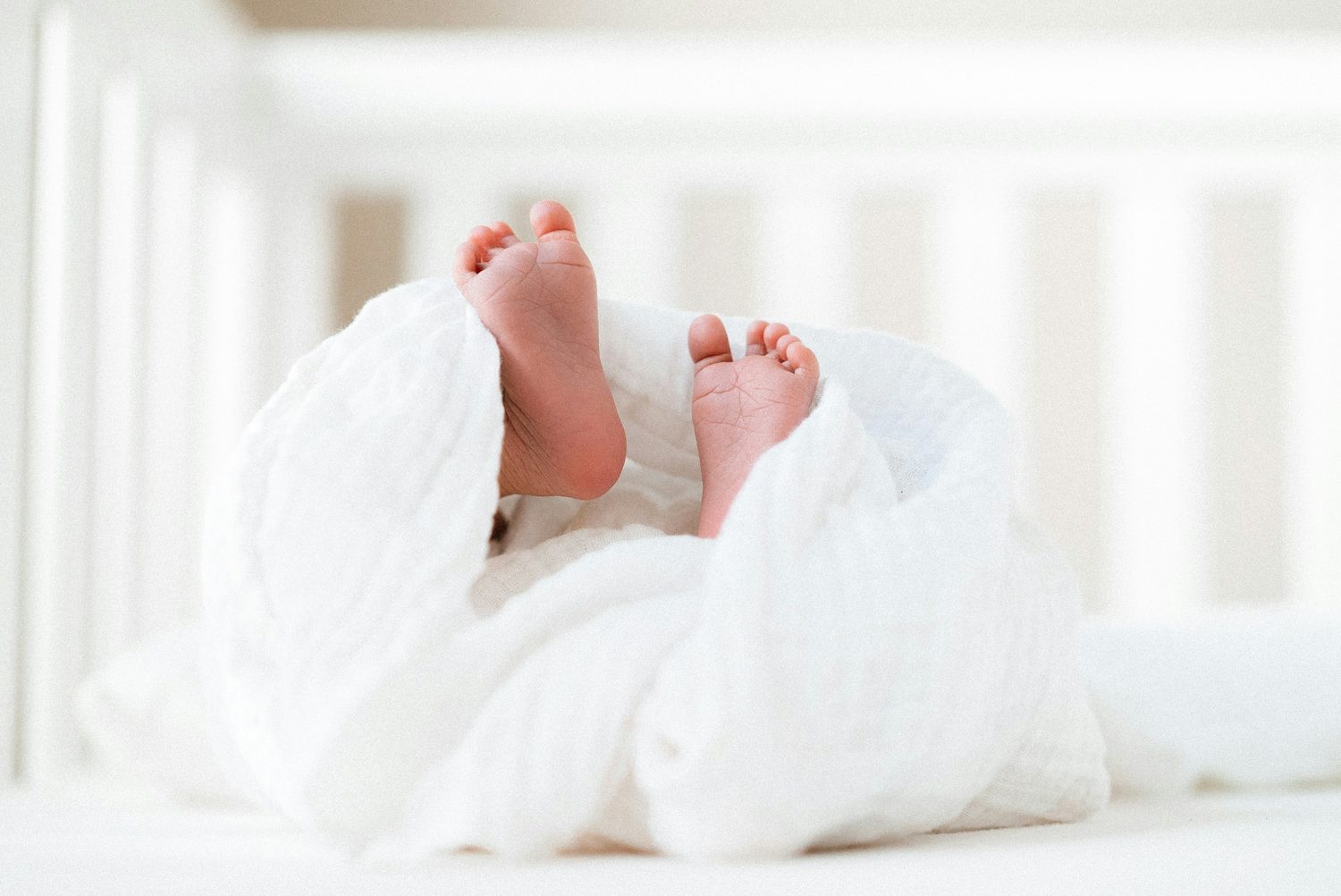 A newborn's feet peeking out from a soft white swaddle
