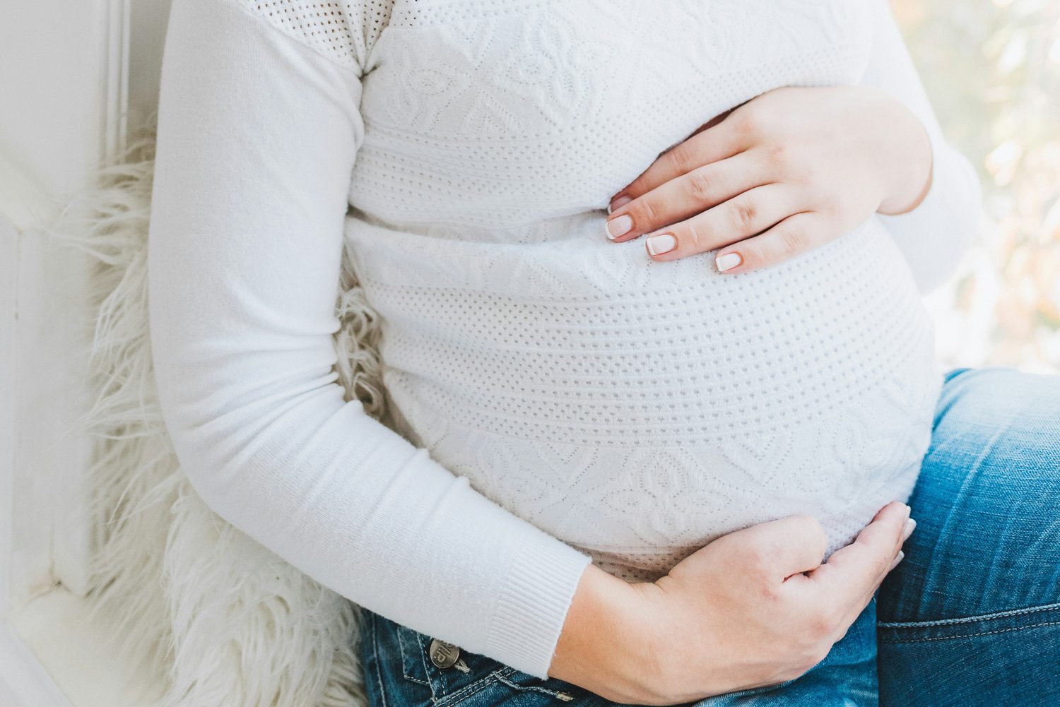 An expecting mother resting her hands on her pregnant belly by a sunlit window